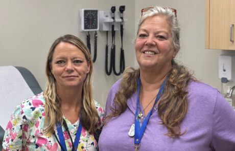 Two women in medical scrubs standing in a doctors office.