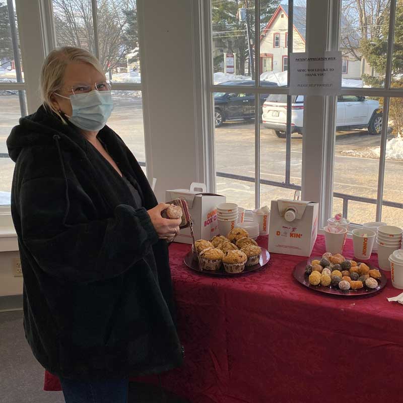 Woman with mask standing in front of table with donuts and coffee