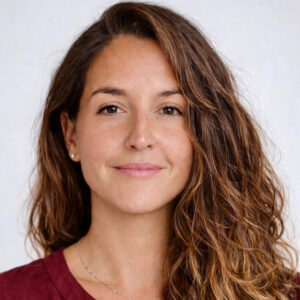 Woman with long wavy brown hair, wearing a maroon top, smiles softly at the camera against a light background. Amber Ives, FNP, Woman with long wavy brown hair, wearing a maroon top, smiles softly at the camera against a light background.