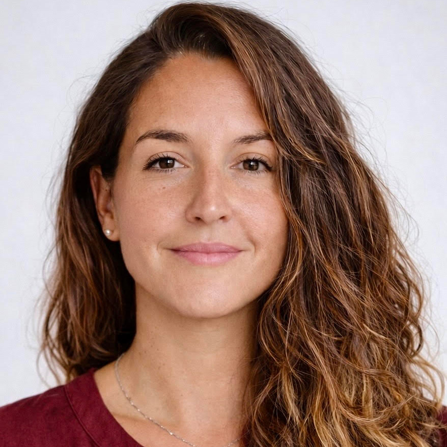 Amber Ives, FNP, Woman with long wavy brown hair, wearing a maroon top, smiles softly at the camera against a light background.