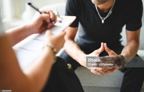 A person writing on a clipboard while seated across from another person.